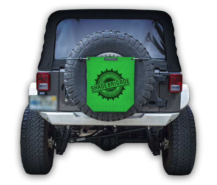 Jeep with Green Buggy Bag on rear tire with a Black Shadebrigade logo in center of it being held up with a trail cord around tire.