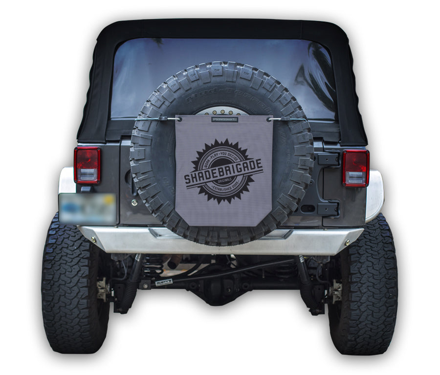 Jeep with Grey Buggy Bag on rear tire with a Black Shadebrigade logo in center of it being held up with a trail cord around tire.