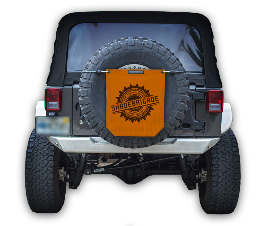 Jeep with Orange Buggy Bag on rear tire with a Black Shadebrigade logo in center of it being held up with a trail cord around tire.