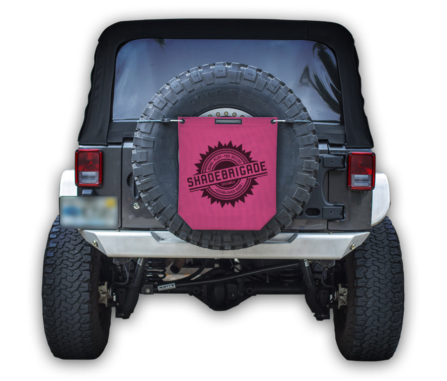 Jeep with Pink Buggy Bag on rear tire with a Black Shadebrigade logo in center of it being held up with a trail cord around tire.