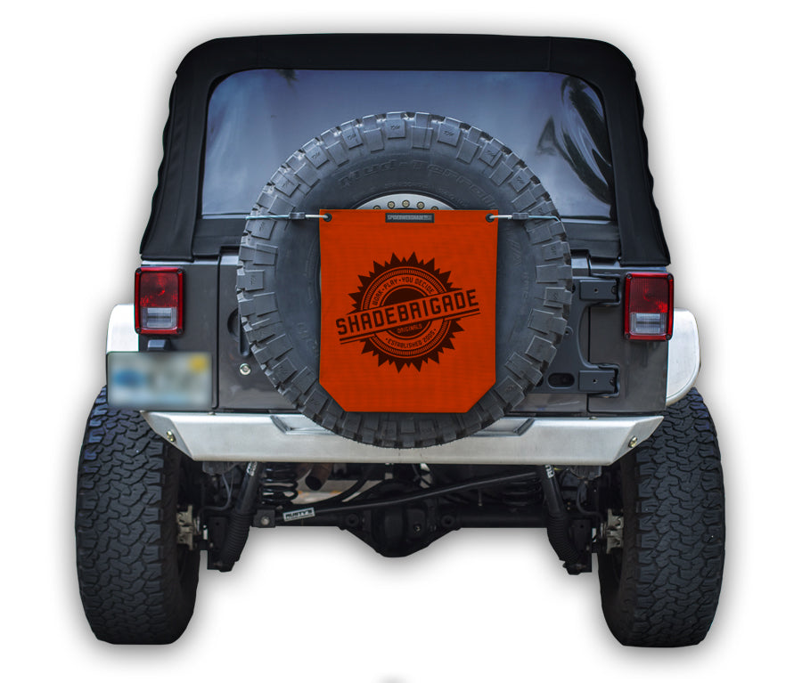Jeep with Red Buggy Bag on rear tire with a Black Shadebrigade logo in center of it being held up with a trail cord around tire.