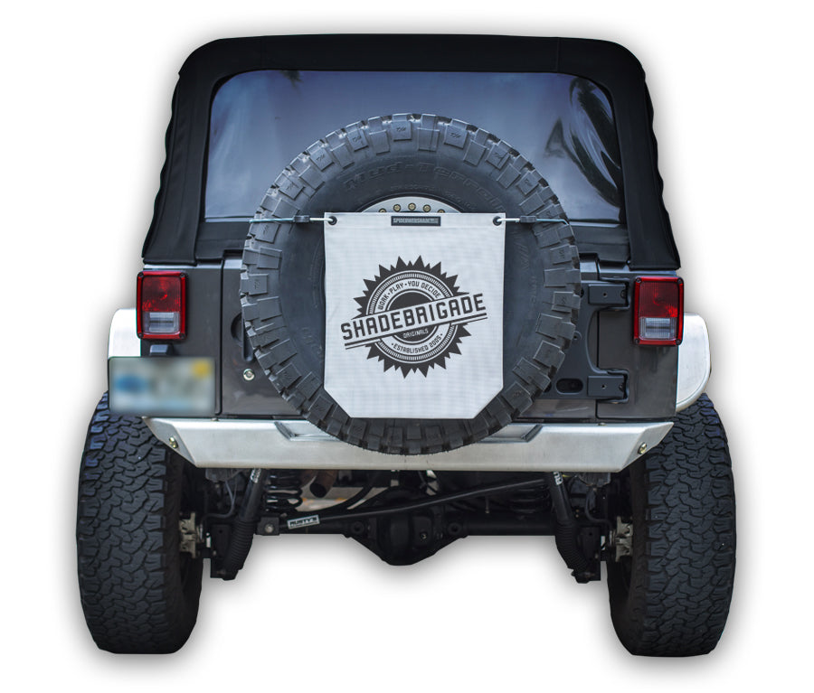 Jeep with White Buggy Bag on rear tire with a Black Shadebrigade logo in center of it being held up with a trail cord around tire.