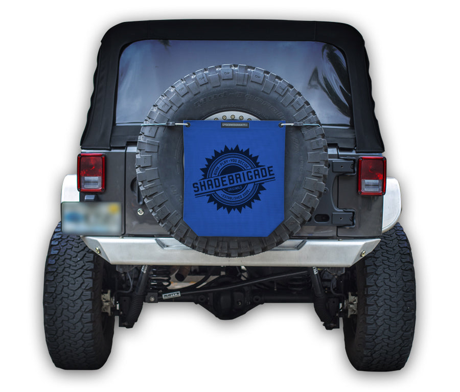 Jeep with Blue Buggy Bag on rear tire with a Black Shadebrigade logo in center of it being held up with a trail cord around tire.