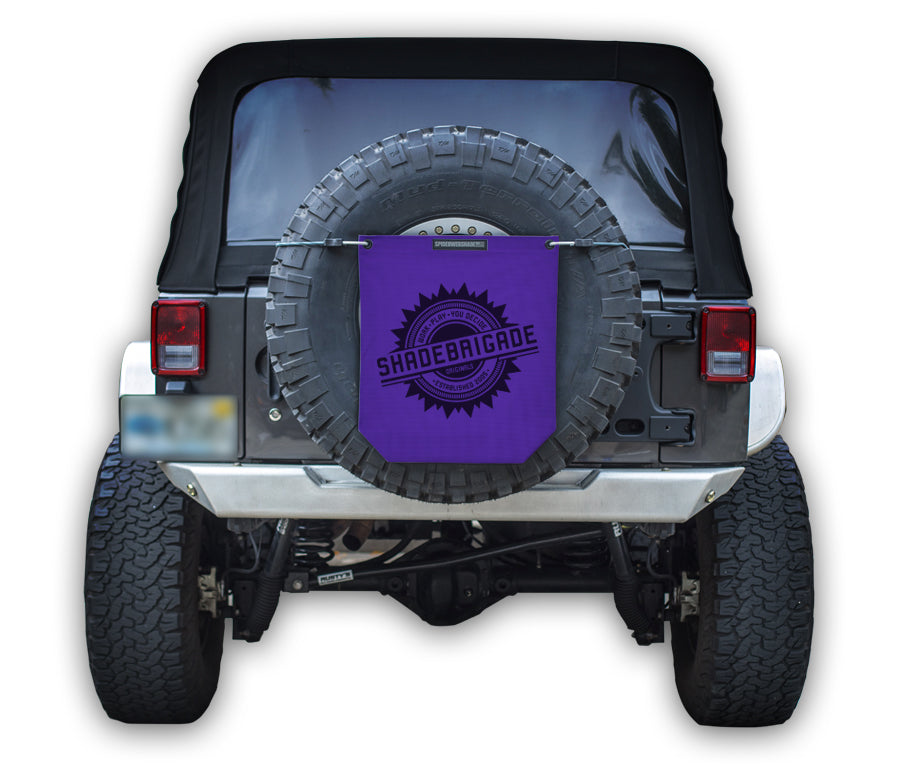 Jeep with Purple Buggy Bag on rear tire with a Black Shadebrigade logo in center of it being held up with a trail cord around tire.