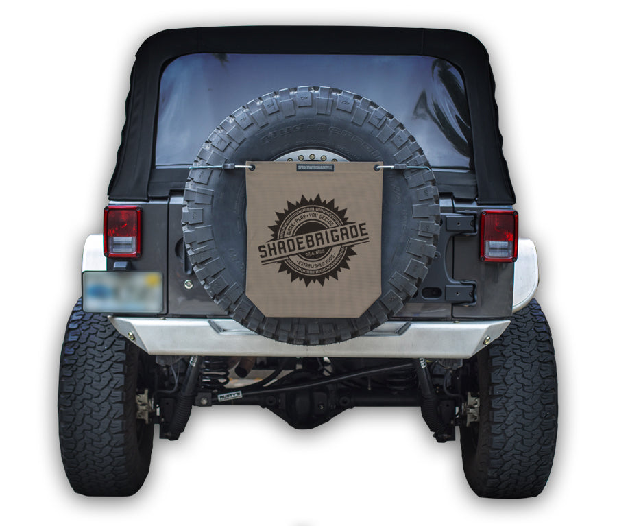 Jeep with Tan Buggy Bag on rear tire with a Black Shadebrigade logo in center of it being held up with a trail cord around tire.