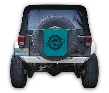 Jeep with Teal Buggy Bag on rear tire with a Black Shadebrigade logo in center of it being held up with a trail cord around tire.