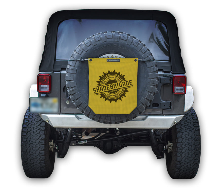 Jeep with Yellow Buggy Bag on rear tire with a Black Shadebrigade logo in center of it being held up with a trail cord around tire.